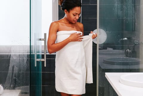 Young African American woman standing in her bathroom wrapping herself with a towel after a shower