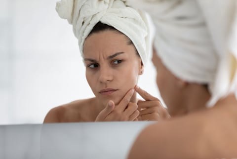 woman popping pimple in mirror