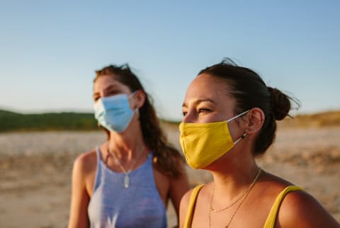 Two Women In Facemasks On The Beach