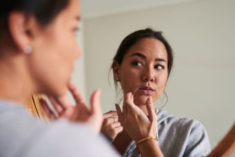 woman picking at skin in mirror