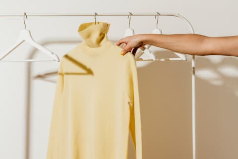 Hand Reaching for a Yellow Turtleneck in a Minimal Closet
