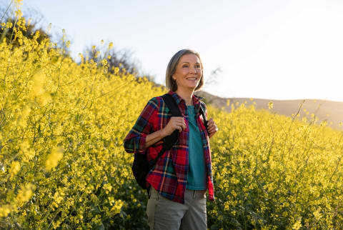 Older woman hiking in flannel among yellow flowers poses for photo