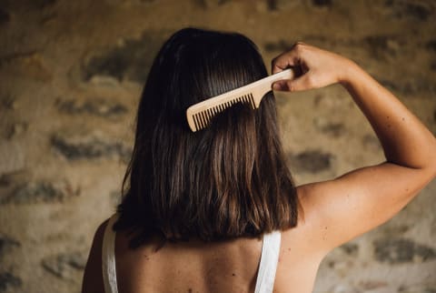 Anonymous woman in white blouse combing her hair, indoor beauty photo shoot.