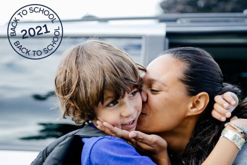 Mother kissing her son on the cheek and cupping his chin with her hand as she drops him off for school.