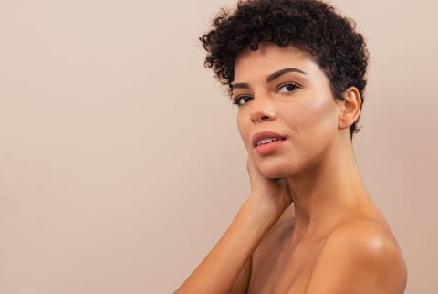 woman touching her face on a tan background 