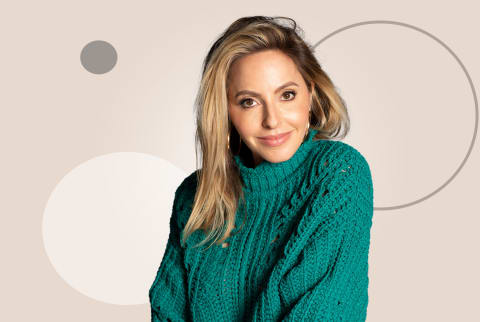 Gabby Bernstein wearing a green sweater and gold hoops, with a neutral background. 