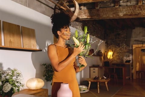 woman in dress smelling a bouquet of flowers in a chic home