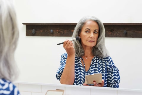 Older woman applies makeup in bathroom mirror