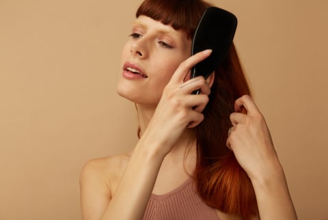 woman with red hair brushing it with a comb