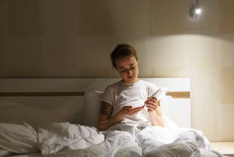 Woman applying hand lotion in bed, evening