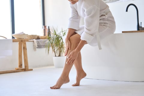 Middle aged mature woman applying veins crème on legs sitting in bathroom. stock photo Middle aged mature woman applying veins crème on legs sitting in bathroom. stock photo