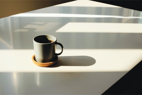White table with cup of coffee in a grey mug on a mustard-colored coaster