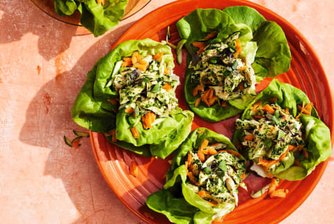 Orange and yellow plates with lettuce wraps and a small white bowl of pesto on a peach colored table cloth