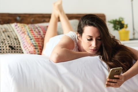 Pretty Brunette Girl Using Mobile Phone On Bed.