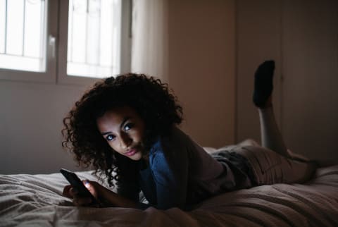 woman in bed on cell phone smirking at camera