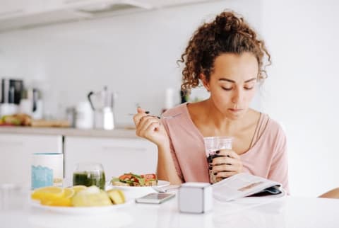 woman eating breakfast and reading in kitchen