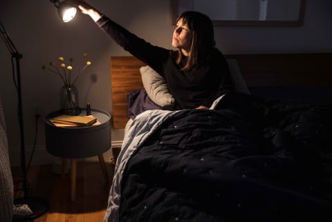Woman sitting in bed turns out lamp to go to sleep