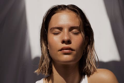 Woman with short blonde hair, closed eyes and glowing skin in direct sunlight