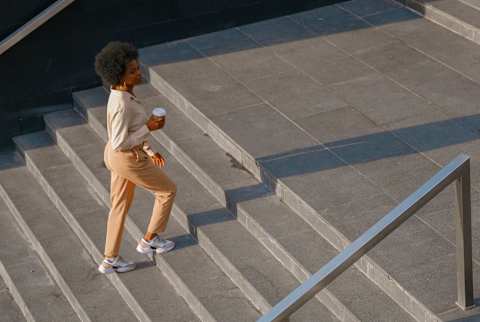 woman walks up stairs outside holding a coffee