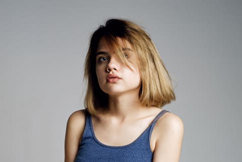  Portrait of beautiful teen girl in blue crop top and grey skirt embracing herself with hand and looking at camera