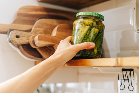 Hand Reaching For a Jar of Pickles on a Kitchen Shelf