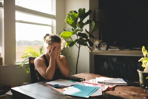 woman with hands over her eyes sitting at a desk