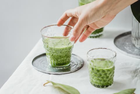 Hand Reaching for a Glass of Green Juice