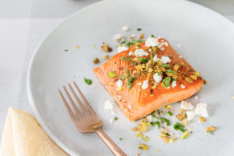 Filet of salmon on a white plate with feta and pistachios and a rose gold fork