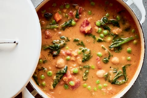 White dutch oven with vegan tomato broth soup with chickpeas, kale, lentils and more veggies.