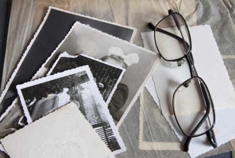Old black and white photographs and a pair of reading glasses on a wooden surface