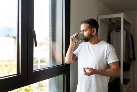 Man taking a supplement with water looking out window