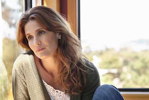 Depressed Woman Looking Out The Window In Her Home