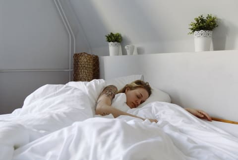 young woman sleeping in white bedroom with plants over bed