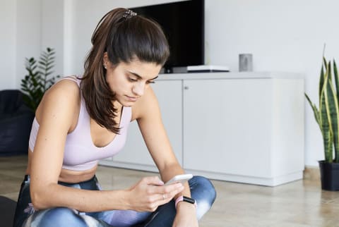 woman sitting on the living room floor with phone about to workout 