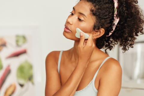 woman using a jade gua sha stone on her cheekbone