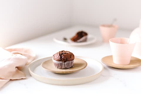 Chocolate muffin on wood plate and white ceramic plate with fork on a table sprinkled with sea salt and accompanied with tea