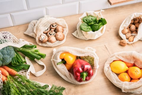 eusable bags with fresh healthy vegetables and fruit on wooden table in the kitchen.