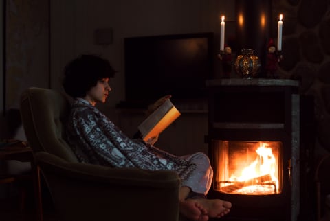 Young Woman Is Reading Book Near The Fireplace