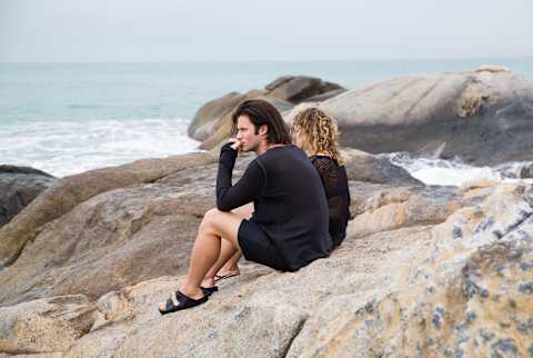 man and woman sitting on rocks looking out at the ocean