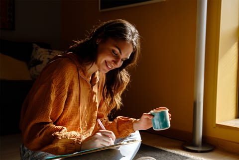 woman handwriting a letter while holding coffee