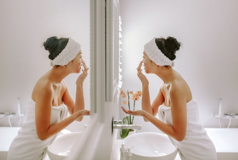 Young woman applying facial cleanser in the bathroom mirror