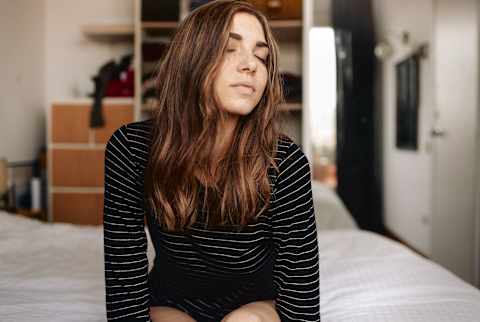 Woman Sitting on the Edge of Her Bed with Her Eyes Closed Woman Sitting on the Edge of Her Bed with Her Eyes Closed