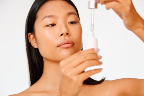 Young Woman with Natural Bright Skin Holding a Serum Bottle