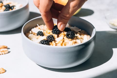 blackberries being topped on an oatmeal breakfast