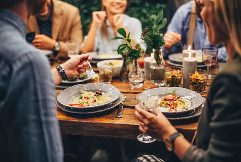 Group of people eating and chatting at outdoors dinner party.