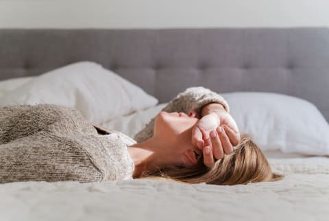 A woman laying in bed covering her face.