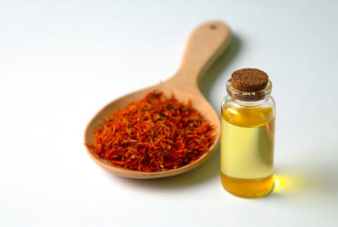 bottle of essential oil and Safflower False Saffron, Saffron Thistle in wooden spoon on white background