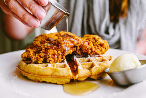 Woman Drizzling Syrup over Chicken and Waffles