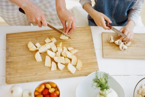 mother and young daughter chop fruits and vegetables in kitchen