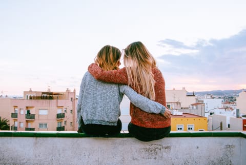 Two Young Women Embracing While Sitting on the Roof